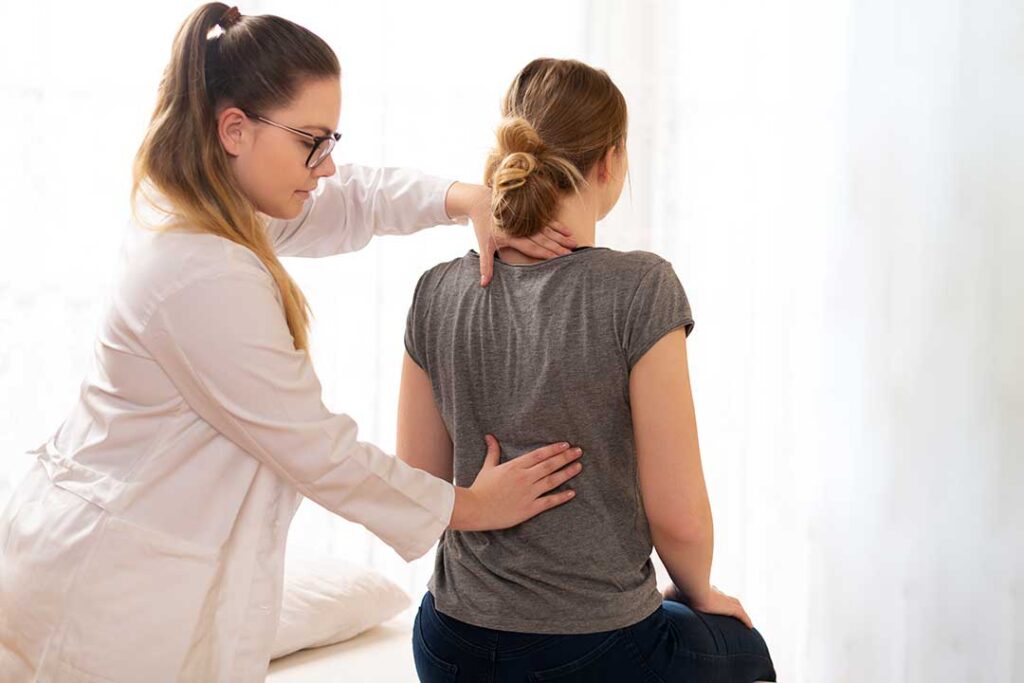 Adult seated beside a wall while a clinician performs a careful balance and neck movement assessment.